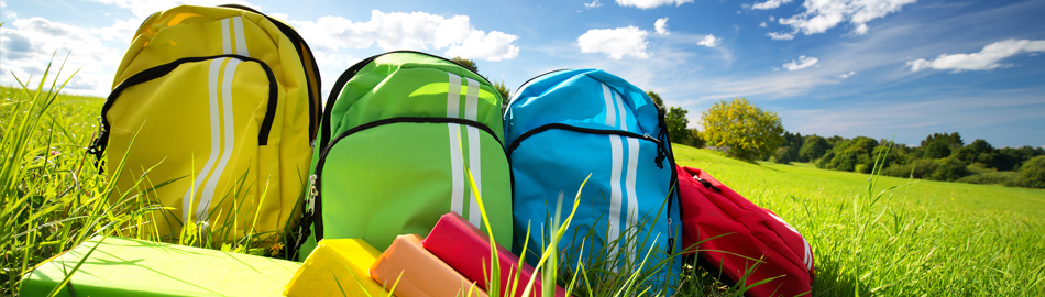 Yellow, green, and blue student backpacks in a field of grass